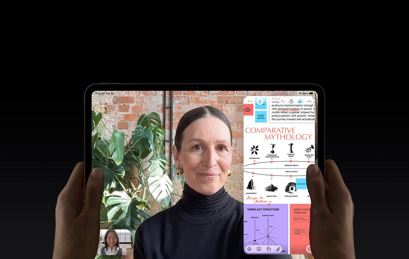 iPad Pro, face avant, noir sidéral, mains gauche et droite tenant l’appareil en orientation paysage, angles arrondis, cadre d’écran noir, écran affichant une conversation FaceTime traduite en direct et une app éducative montrant une présentation de la mythologie comparée avec du texte, des diagrammes et des notes manuscrites