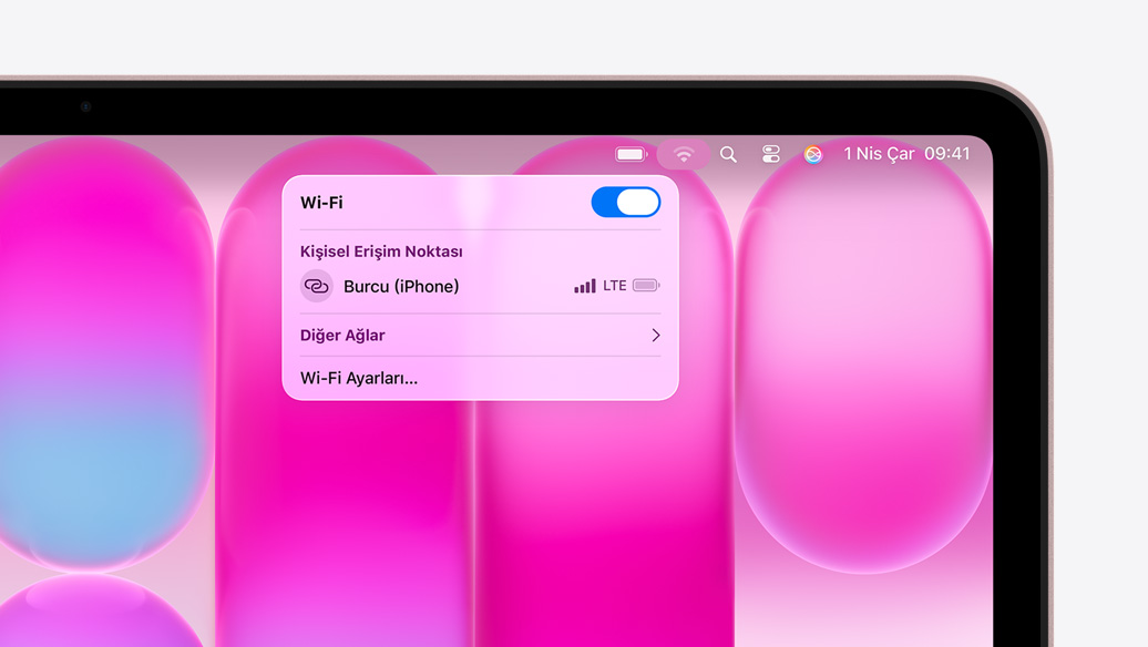 MacBook Neo, pastel pembe renk, Wi-Fi menüsünde Kişisel Erişim Noktası bölümü ve “Burcu (iPhone)” seçeneği gösteriliyor