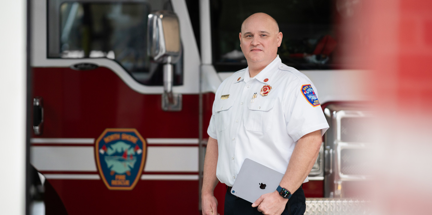 Le chef des pompiers se tient devant un camion de pompiers avec un iPad à la main et une Apple Watch au poignet